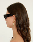 Woman wearing black sunglasses and gold earrings against a white background