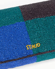 Close-up of a beaded clutch with a colorful pattern and 'Staud' branding.