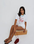 model sitting while wearing sea la ie graphic tee with a turquoise necklace on a white background