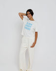 model wearing aloha howdy cheers short sleeve tee with white pants on a white background