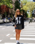 Woman wearing a black sweatshirt with 'NY 78' text on a city street, full body view