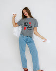Person wearing a gray t-shirt with text and red hearts, blue jeans, and red shoes on a white background, full body view