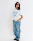 Person wearing a white t-shirt with blue text and light blue jeans on a white background, side