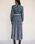 Woman wearing a blue floral dress with a belt against a white background, back