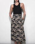 Woman wearing a black sleeveless top and a long, patterned skirt on a white background