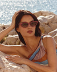 Solange Sunglasses Scarlet Chroma + Bordeaux on model with average, square face shape, laying on rocks by the sea