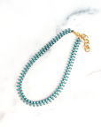 Turquoise beaded necklace with a gold clasp on a white marble surface