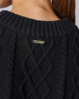 Close-up back view of a person wearing a black cable-knit sweater, showing the neck and upper back with a small metal brand tag reading 'CLEOBELLA' at the center.