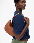 Woman wearing a blue knitted sweater with a colorful beaded accessory, holding a brown woven handbag.