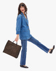 Woman in a denim outfit holding a leopard print bag on a white background