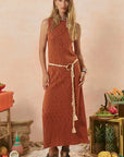 Woman wearing a rust-colored dress with tassels in a rustic setting