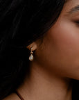 Close-up of a woman wearing a gold earring with a teardrop-shaped gemstone.