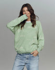 Woman wearing a light green sweatshirt with text and blue jeans on a gray background
