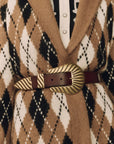 A close-up of a brown leather belt with a large, ornate gold-toned buckle, worn over a tan, black, and white argyle knit cardigan.