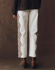 Person wearing wayne jeans with decorative trim and brown boots against a brown background, back