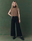 Woman wearing a brown sleeveless top and black pants against a green background
