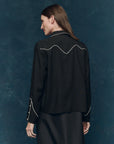 Woman wearing the western shirt with black outfit with white accents and sunglasses against a plain background, back view