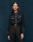 Woman wearing the western shirt black blouse with white embroidery against a dark blue background