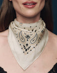 Woman wearing a beige bandana with black paisley pattern