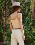 Woman wearing a beige hat, the Henley Slim Tank Stripe, and white pants standing in a garden, back view