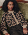 model wearing the leopard windsor cardigan with jeans cream sitting on a green chair