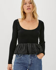 Woman wearing a black long-sleeve top with a peplum waist and blue jeans on a white background front view