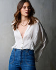 Woman wearing a white blouse and blue jeans against a gray background