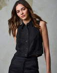 Woman wearing a black sleeveless blouse with pleated details against a neutral background