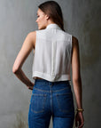 Person wearing a white sleeveless shirt and blue jeans against a gray wall, back view