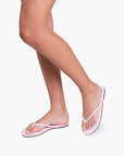 Pink flip-flops worn on feet against a white background