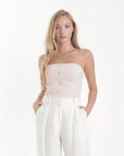Woman wearing a strapless top and white pants on a white background