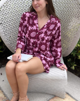 Woman in a pink and purple patterned pj set sitting on a white chair outdoors.