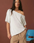 Woman wearing a white off-shoulder top and brown pants against a brown background