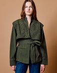 Woman wearing a green jacket with intricate detailing on a brown background