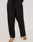 Black wide-leg drawstring pants shown on a model from the waist down, paired with black heeled sandals against a plain light gray studio background.
