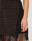 model wearing a fringe plaid skirt with a grey top, loafers, on a light grey background