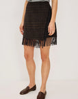 model wearing a fringe plaid skirt with a grey top, loafers, on a light grey background