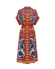 A short-sleeved midi dress with a high collar and a self-tie waist, featuring a vibrant orange-red base with a multicolor bohemian floral and geometric print, shown from the back against a plain white background.