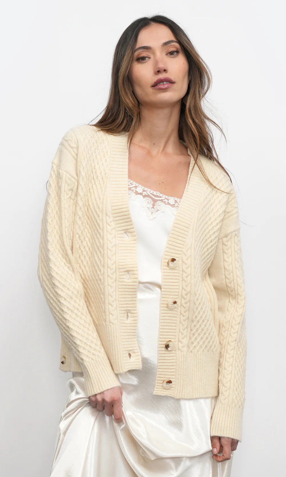 Woman wearing a cream-colored cardigan over a white dress on a plain background