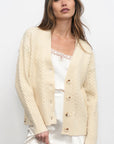 Woman wearing a cream-colored cardigan over a white dress on a plain background