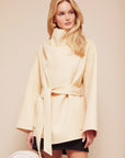 Woman wearing a light yellow coat against a beige background front view