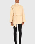 Woman wearing a beige coat, black pants, and black boots on a white background front view