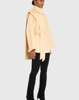 Woman wearing a beige coat, black pants, and high-heeled shoes on a white background side view
