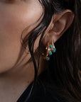 Close-up of a woman wearing gold earrings with turquoise stones.