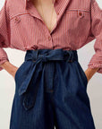 A close-up of a person wearing a red and white vertically striped button-up shirt and dark blue high-waisted denim culottes with a matching tie belt.