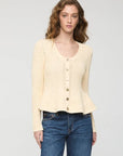 A woman modeling a cream-colored, textured knit cardigan sweater with button-front closure, paired with blue jeans, against a plain light gray studio background.