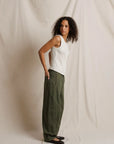 Woman wearing a white sleeveless top and green pants against a plain background