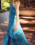 Woman in a blue floral dress standing on a tiled patio, side