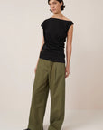 asymmetric top in black on a model with green pants on a cream background
