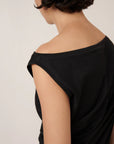 asymmetric top in black on a model with green pants on a cream background, shoulder view